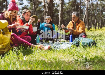 Uomini e donne sorridenti che mangiano cibo seduto nella foresta in giorno di sole Foto Stock