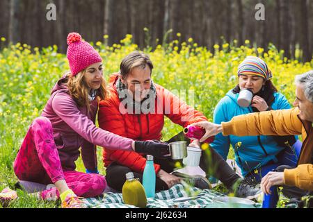 Uomo maturo che versa caffè a donna seduto con gli amici nella foresta Foto Stock