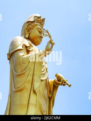 La grande statua d'oro di Guan Yin, cielo blu d'estate con forte luce solare, immagine verticale di Guan Yin d'oro. Foto Stock