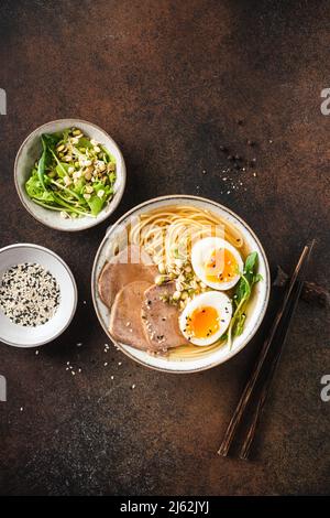 Ciotola per zuppa di ramen con uova e carne su sfondo marrone scuro, vista da tavolo. Cucina asiatica Foto Stock