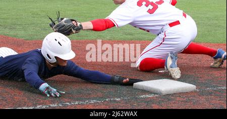 Il giocatore di baseball scivola la testa prima nella terza base evitando il tag durante un primo piano di gioco della scuola superiore. Foto Stock