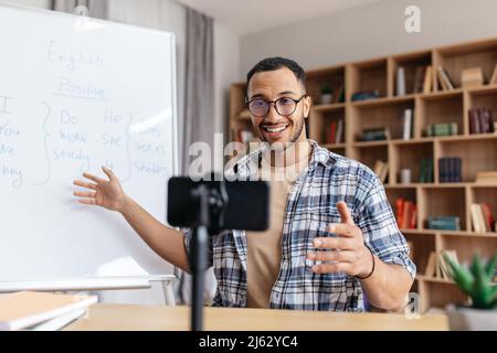 Felice bel tutor arabo maschile che mostra le regole dell'inglese e guardando lo smartphone in casa ufficio interno Foto Stock
