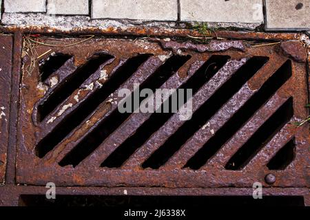 Un vecchio manhole arrugginito per ricevere acqua piovana o neve fusa. Sullo sfondo di lastre di pavimentazione grigie. Vista dall'alto Foto Stock