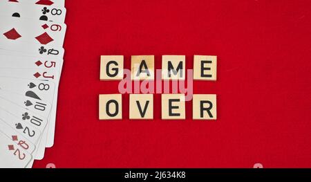 Frase "Game Over" composta da tavole di legno e carte da gioco su sfondo rosso feltro Foto Stock