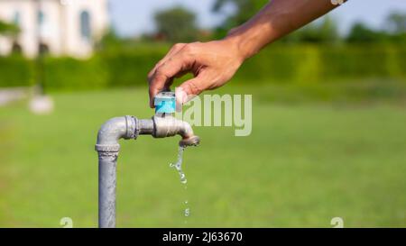 La mano maschio apre il rubinetto d'acqua del giardino, versando acqua pulita rubinetto d'acqua dolce, attivare il rubinetto, mani-fuori acqua, . Foto Stock