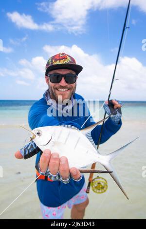 Un pescatore sorridente che gli fa scorrere il pescato su una spiaggia caraibica. Foto Stock