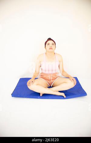 giovane donna in posa yoga con testa sollevata e occhi aperti su tappeto blu con fondo bianco Foto Stock