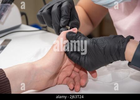 Rimozione della cuticola con tagliaunghie. Mani con guanti di un manicurista esperto taglio cuticole con pinzette metalliche, primo piano. Mani durante un manicure ca Foto Stock