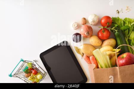 Sfondo concettuale dello shopping online con dispositivi mobili e borsa di shopping al supermercato piena di frutta e verdura. Vista dall'alto. Horizont Foto Stock