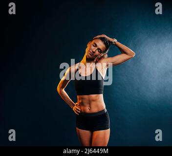 Giovane donna muscolare che scalda il collo prima di allenarsi su sfondo nero Foto Stock