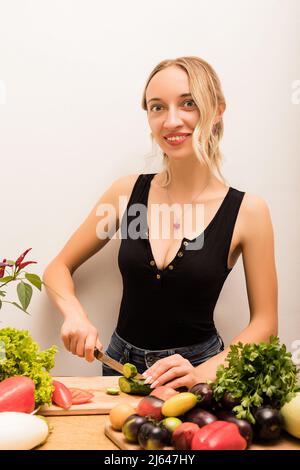 Giovane bella donna taglia le verdure con un coltello in cucina Foto Stock