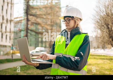 Ingegnere industriale donna in uniforme di lavoro collegato con notebook smart PC in piedi presso il cantiere. Foto Stock