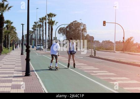 vacanze in vacanza. una donna sui pattini a rotelle e un uomo su uno skateboard si divertono all'aperto in estate giorno di sole. concetto di amore e amicizia. Alto Foto Stock