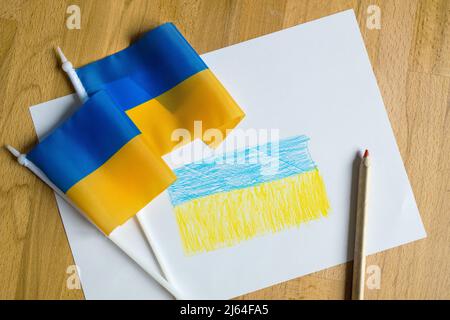 Matita di colore giallo e blu che disegna la bandiera Ucraina sul tavolo interno a casa Foto Stock