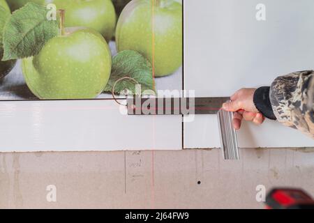 Un uomo che utilizza una livella laser e un righello fa delle marcature per l'apertura di una presa elettrica. Foto Stock