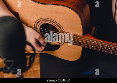 vista dall'alto uomo caucasico irriconoscibile, registrazione di musica con chitarra acustica e microfono sfocato in primo piano, copy space, concetto di corsi di musica. Foto Stock