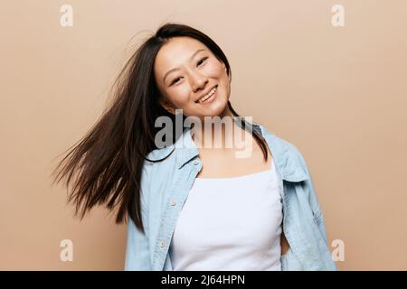 Ballando allegro abbronzato adorabile giovane ragazza asiatica che gira ondeggiando i suoi capelli posa isolato su sfondo beige pastello. Persone ed emozioni. Felicità Foto Stock