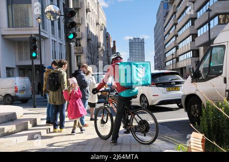 Un maschio Deliveroo cibo corriere cyclist stazionari sulla sua bicicletta in una strada con zaino termico isolato e logo, centro di Londra, Inghilterra, Regno Unito Foto Stock