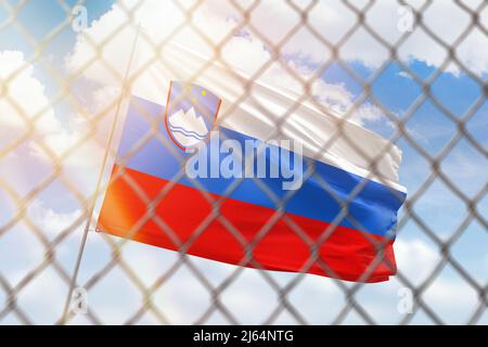 Una rete d'acciaio sullo sfondo di un cielo blu e un flagpole con la bandiera della slovenia Foto Stock