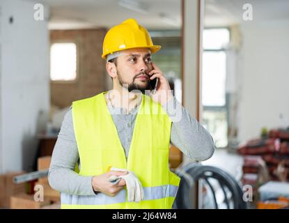 Giovane ingegnere civile bearded che parla al telefono in cantiere Foto Stock