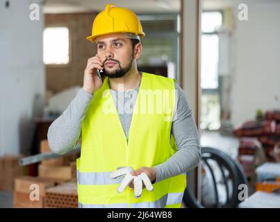 Giovane ingegnere civile bearded che parla al telefono in cantiere Foto Stock