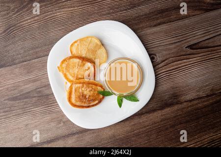 Mucchio di frittelle spesse fritte di fresco, nelle cucine dell'Europa orientale chiamate oladky o oladyi con latte condensato su sfondo di legno. Foto Stock