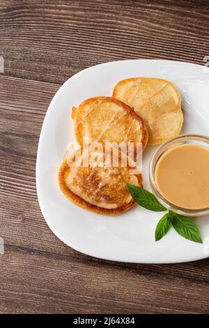 Mucchio di frittelle spesse fritte di fresco, nelle cucine dell'Europa orientale chiamate oladky o oladyi con latte condensato su sfondo di legno. Foto Stock