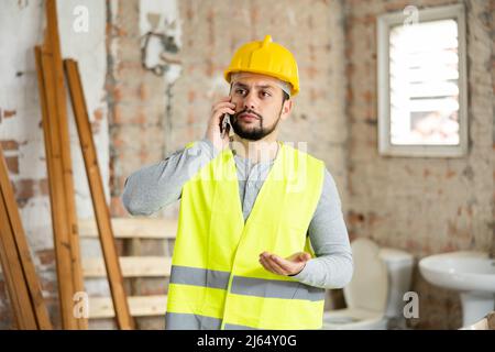 Giovane ingegnere civile bearded che parla al telefono in cantiere Foto Stock