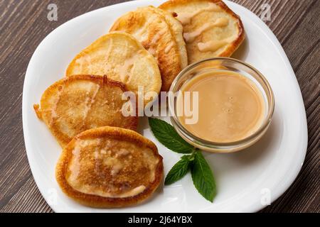 Mucchio di frittelle spesse fritte di fresco, nelle cucine dell'Europa orientale chiamate oladky o oladyi con latte condensato su sfondo di legno. Foto Stock