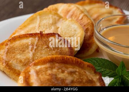 Mucchio di frittelle spesse fritte di fresco, nelle cucine dell'Europa orientale chiamate oladky o oladyi con latte condensato su sfondo di legno. Foto Stock