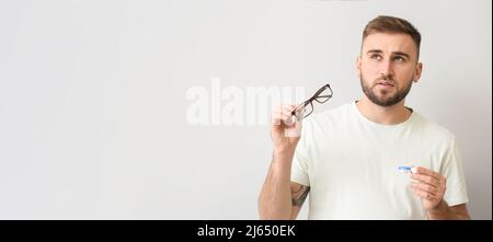 Uomo attento che sceglie tra lenti a contatto e occhiali su sfondo chiaro con spazio per il testo Foto Stock