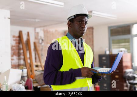 Supervisore afro-americano con computer portatile che ispeziona il cantiere Foto Stock