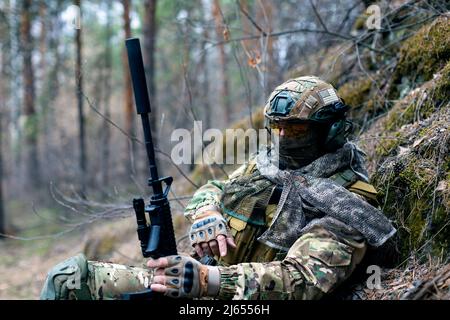 Concetto di guerra moderna - un soldato mercenario sta riposando dopo uno scontro nella foresta. Primo piano di un soldato in camuffamento che si mescola con il en Foto Stock