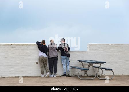 Una donna e due giovani uomini che guardano su una parete di mattoni dipinta di bianco al Nobbys Lighthouse vicino all'entrata del Porto di Newcastle in Australia Foto Stock