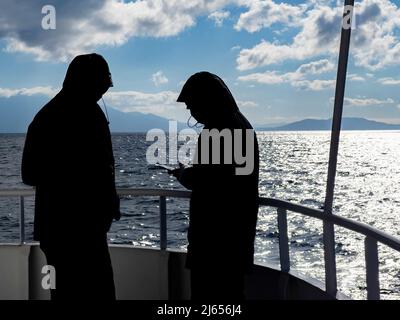 Due persone sul ponte della nave che guardano l'app per telefono cellulare durante il giorno d'inverno soleggiato.domanda di viaggio, prenotazione online dell'hotel, check-in mobile per consigli di viaggio. Foto Stock