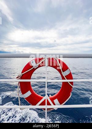 Lifebuoy a righe rosse appeso a bordo della nave. Vista mare. Grande sfondo vuoto con spazio di copia. Concetto di aiuto e sicurezza. Boa salvavita ad anello arancione. Foto Stock