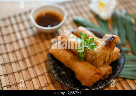 Gustosi involtini primavera di verdure asiatiche su un piatto nero minimale servito con speciale salsa dolce e piccante. Foto Stock