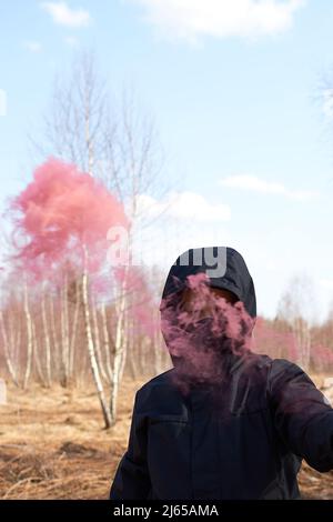 Un preteen in una giacca nera e una maschera tiene una scacchiera con fumo colorato Foto Stock