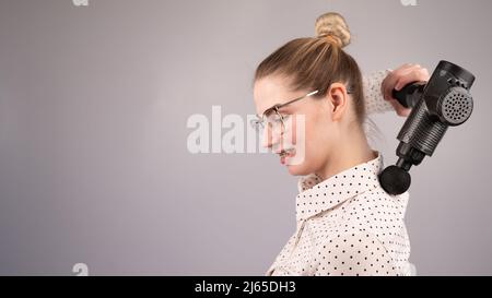 Donna sorridente con bretelle usa una pistola massaggiatore per la schiena. Foto Stock