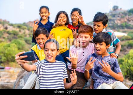 Gruppo di bambini in allegro prendere selfie sul telefono cellulare in cima alla collina dopo aver raggiunto la destinazione in cima alla collina - concetto di amicizia, vacanze, all'aperto Foto Stock