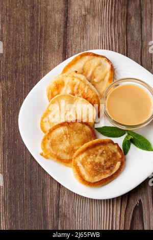 Mucchio di frittelle spesse fritte di fresco, nelle cucine dell'Europa orientale chiamate oladky o oladyi con latte condensato su sfondo di legno. Foto Stock