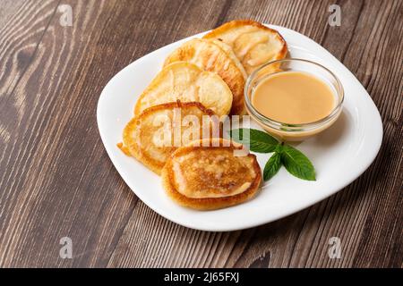 Mucchio di frittelle spesse fritte di fresco, nelle cucine dell'Europa orientale chiamate oladky o oladyi con latte condensato su sfondo di legno. Foto Stock