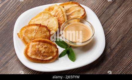 Mucchio di frittelle spesse fritte di fresco, nelle cucine dell'Europa orientale chiamate oladky o oladyi con latte condensato su sfondo di legno. Foto Stock