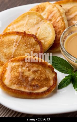 Mucchio di frittelle spesse fritte di fresco, nelle cucine dell'Europa orientale chiamate oladky o oladyi con latte condensato su sfondo di legno. Foto Stock