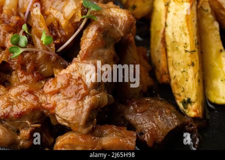 Patate novelle al forno con sale marino e filetto di maiale tagliato a pezzi in un piatto nero, su tavola di marmo Foto Stock