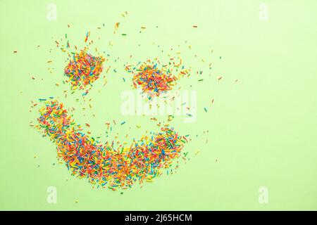 Emoji sorridenti fatte di dolci e colorati spruzzi di zucchero su sfondo verde con spazio libero copia. Foto Stock