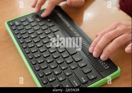 Un uomo cieco utilizza un computer con un display Braille e una tastiera per computer. Dispositivo incluso. Foto Stock