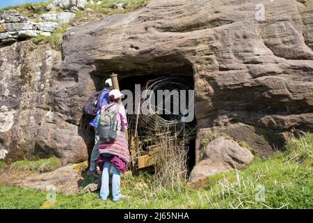 Escursionisti che ispezionano l'ingresso di un 18th secolo scavato byre sopra Ravenstonedale, Upper Lune Valley, Yorkshire Dales National Park, Regno Unito Foto Stock