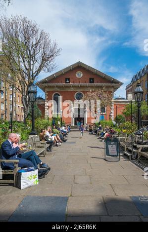 Persone sedute su panchine socializzanti e rilassanti nel giardino della Chiesa di San Paolo a Covent Garden in una soleggiata primavera. Londra, Inghilterra, Regno Unito. Foto Stock