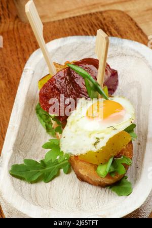 Deliziose tapas spagnole con uova di quaglia fritte, chorizo arrosto e patate con cipolla verde su Baguette pane primo piano su sfondo di legno Foto Stock